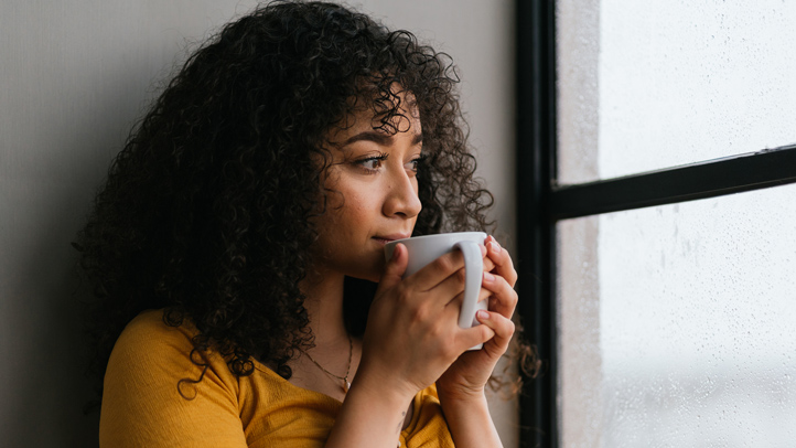 woman sipping from a coffee mug while looking out the window
