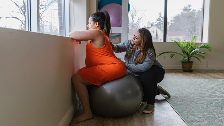 birthing ball, pregnant woman sitting on birthing ball next to doula