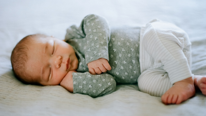 newborn scrunch, newborn baby dressed in a green shirt and white pants sleep on her side on a white sheet