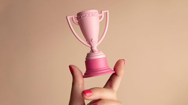 potty training rewards, hand holding a small pink trophy in front of a beige background