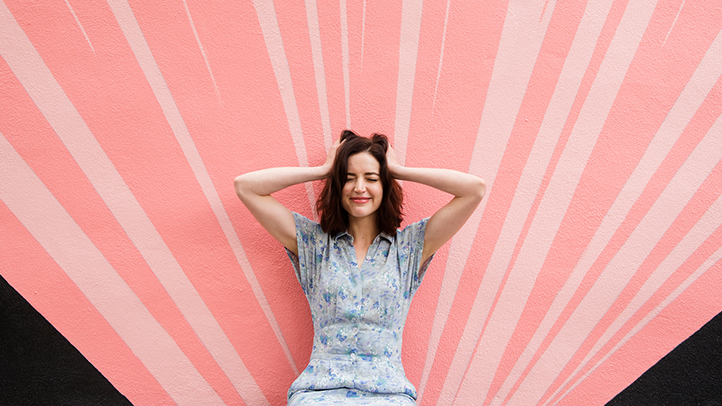 stress during pregnancy, woman holding her hands to her head in front of a pink wall