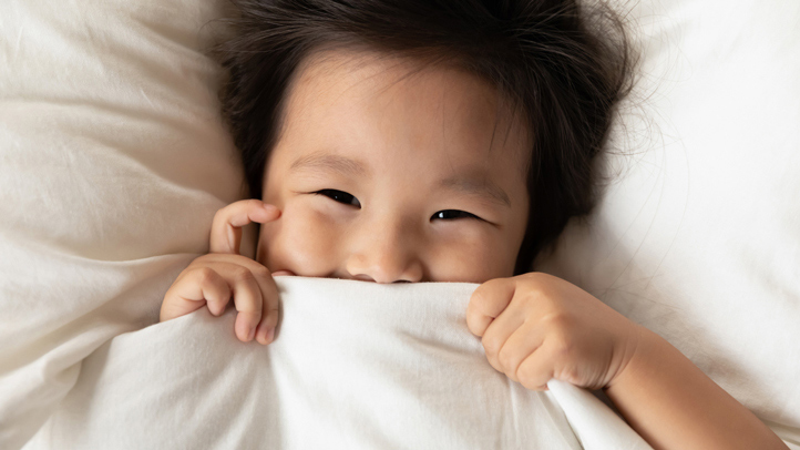 sleep regression in toddlers, smiling toddler under covers