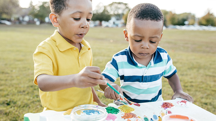 toddler summer camp, two toddler boys at an art table out on a field