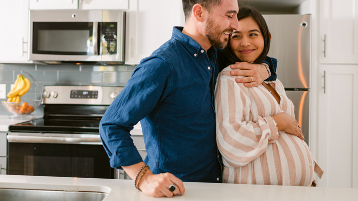 twin pregnancy weight gain, happy pregnant couple embracing in kitchen