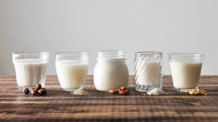 types of milk for babies and toddlers by age, different kinds of milk in glasses with different fruits and vegetables and nuts in front